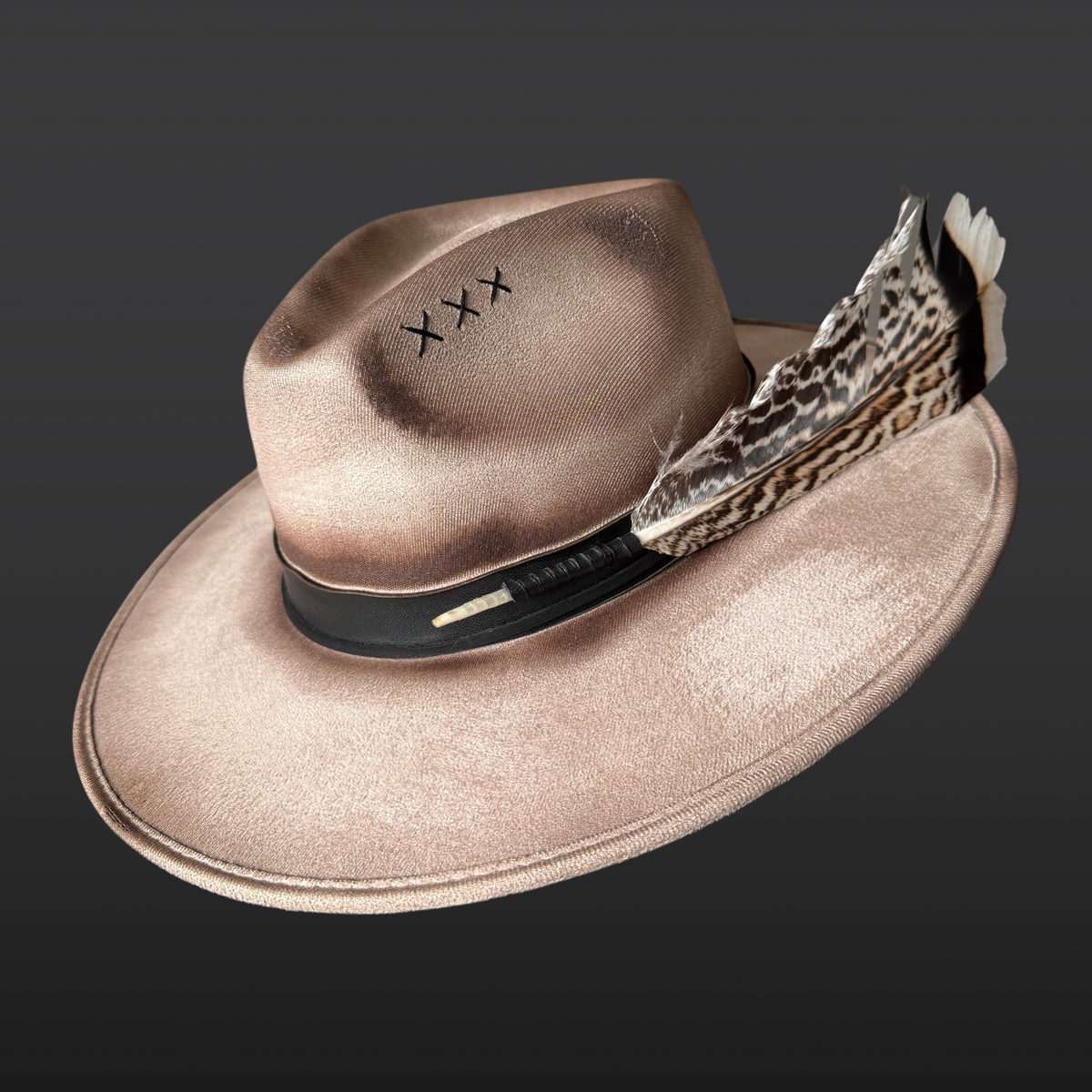 Side view:
A wide-brimmed khaki fedora shown from the side, featuring a hand-torched textured finish, black leather band, chalcopyrite crystal, and feather accents.