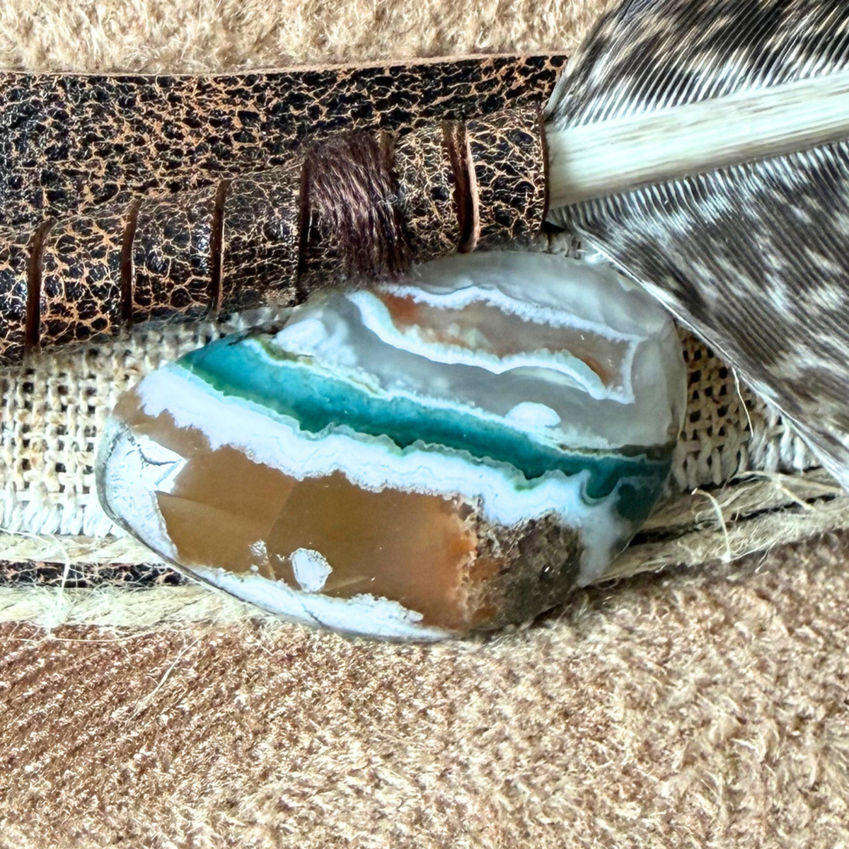 A close-up of the agate stone attached to the dark brown leather band of a camel-colored wide-brimmed fedora.