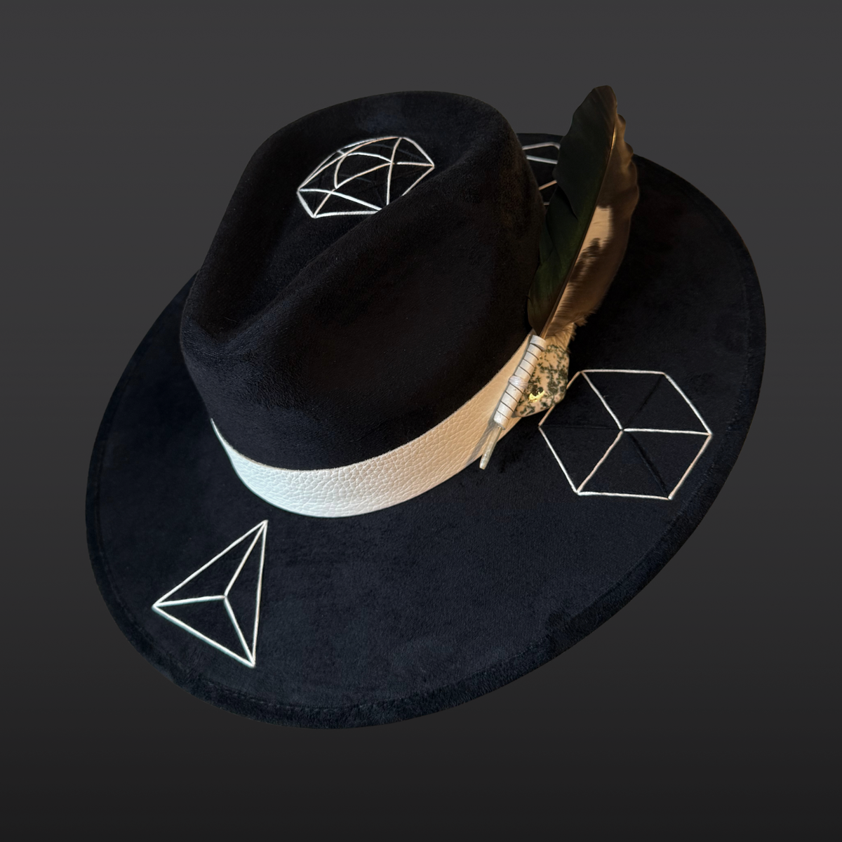Left Side view:
A wide-brimmed black fedora shown from the side, featuring a white leather band, green tree agate crystal, and multicolored duck feather accent.