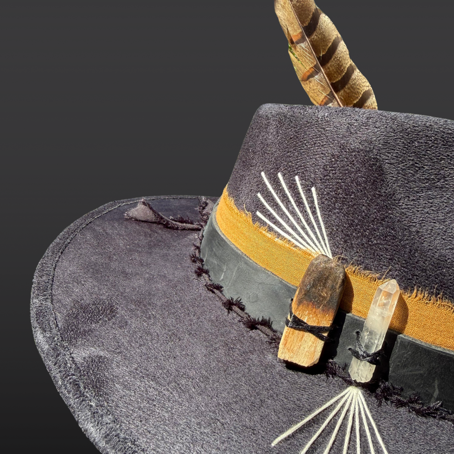 Close-up of Lemurian quartz crystal and naturally burnt palo santo attached to black vegan suede fedora with leather band details.