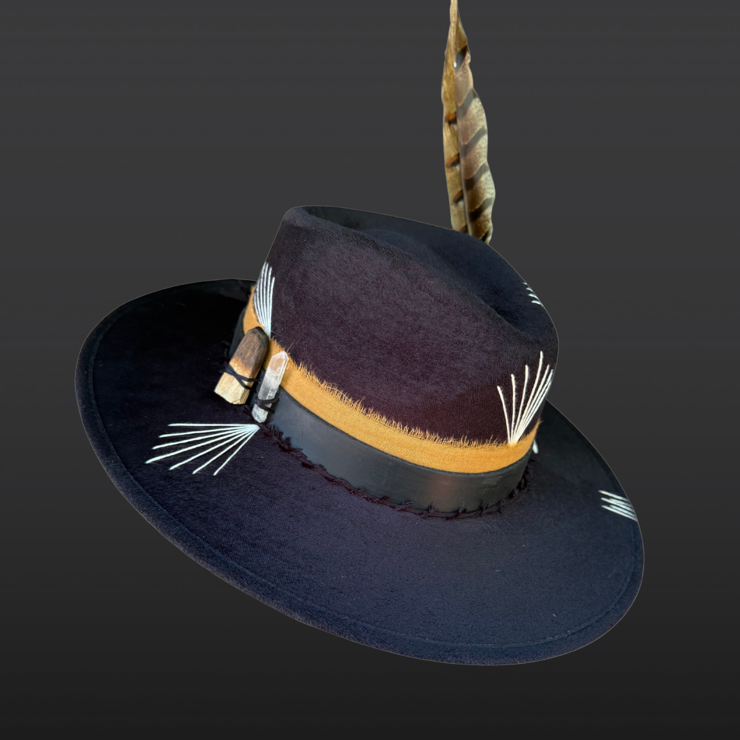 Black vegan suede fedora showing hand embroidered sunburst details, layered leather and cotton bands, and natural feather accent.