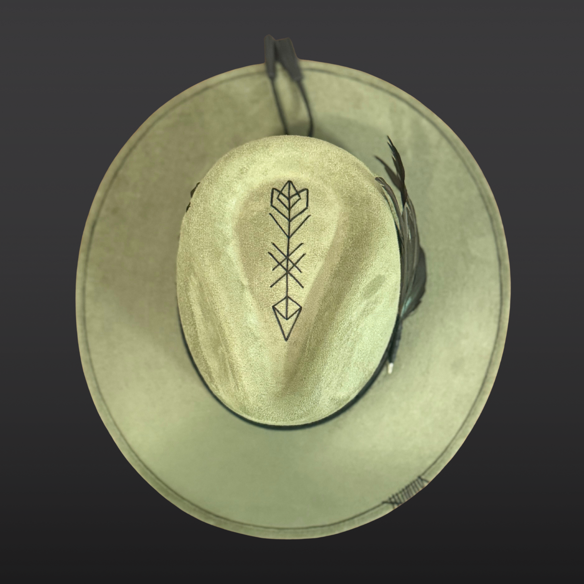 Top view of sage green Flecha fedora with embroidered arrow, black obsidian arrow stone and rooster feathers