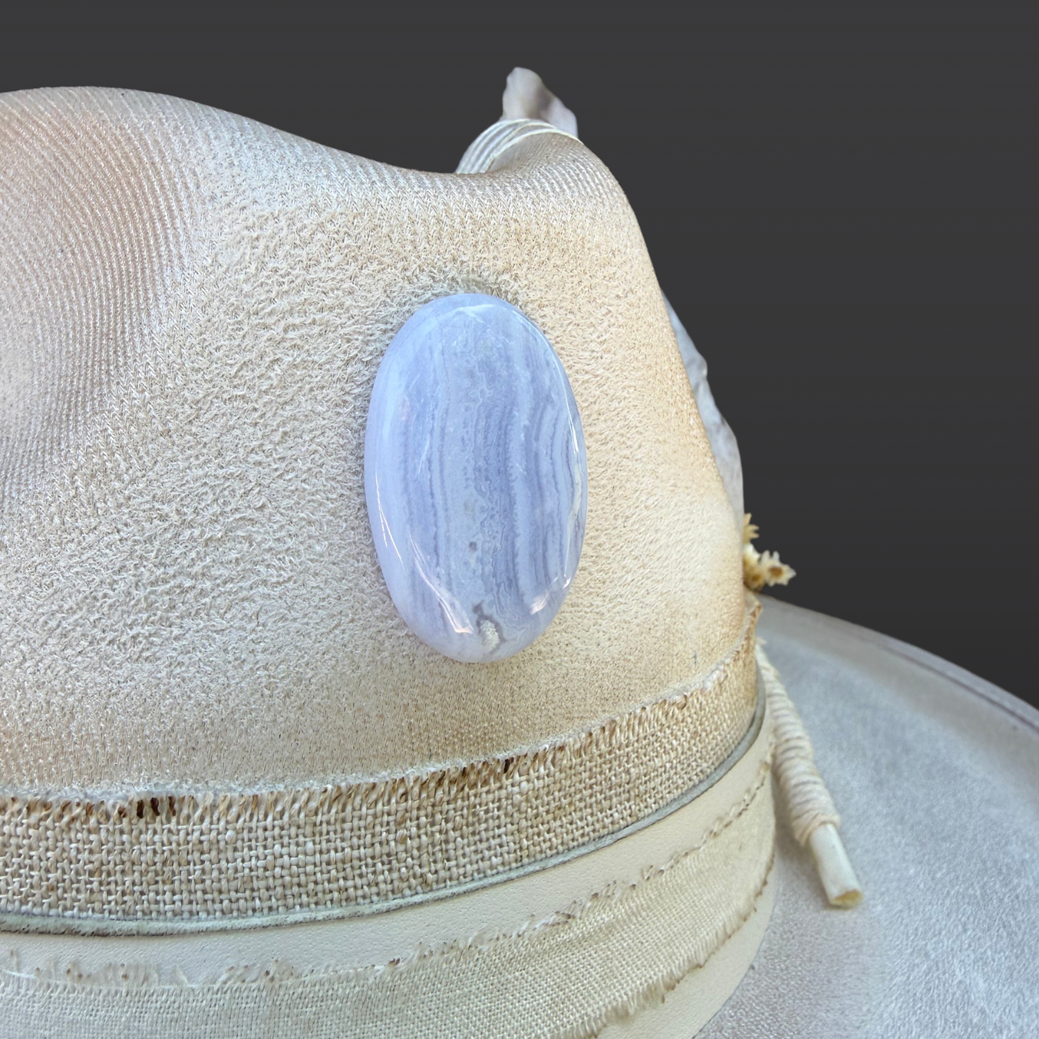 Close-up of blue lace agate crystal attached to ivory fedora with handcrafted leather details and embroidered accents.