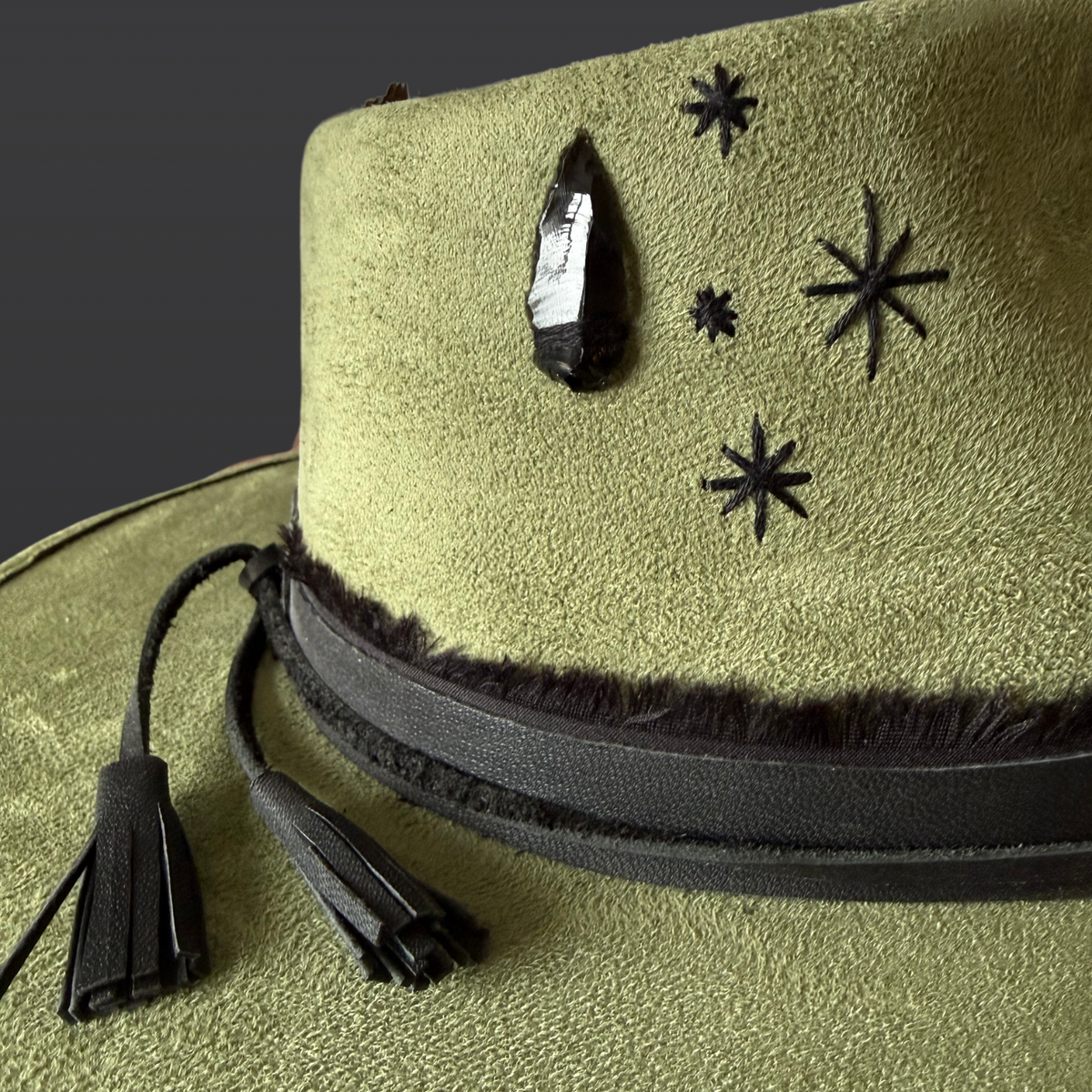 Detail view: Close-up of the hand-embroidery and black obsidian arrow stone on a sage green fedora.