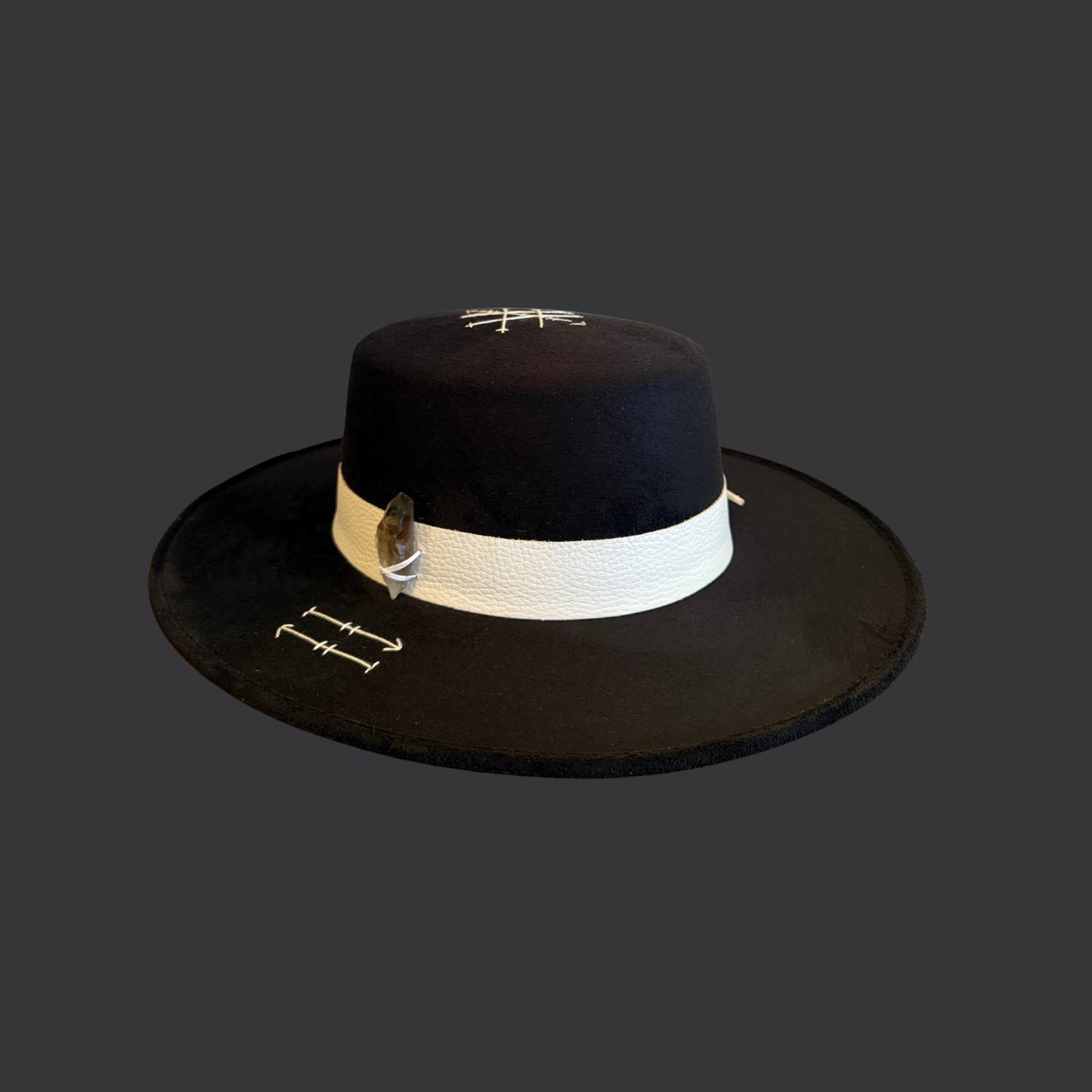 Black vegan suede Cordobes flat top fedora hat with smoky quartz crystal, arrow embroidery, white leather band, and turkey feather / front view