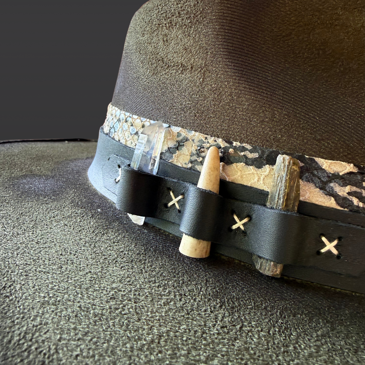 Close-up of green kyanite, Lemurian quartz, deer antler, and serpent-print leather accents on the Verdant Viper fedora.