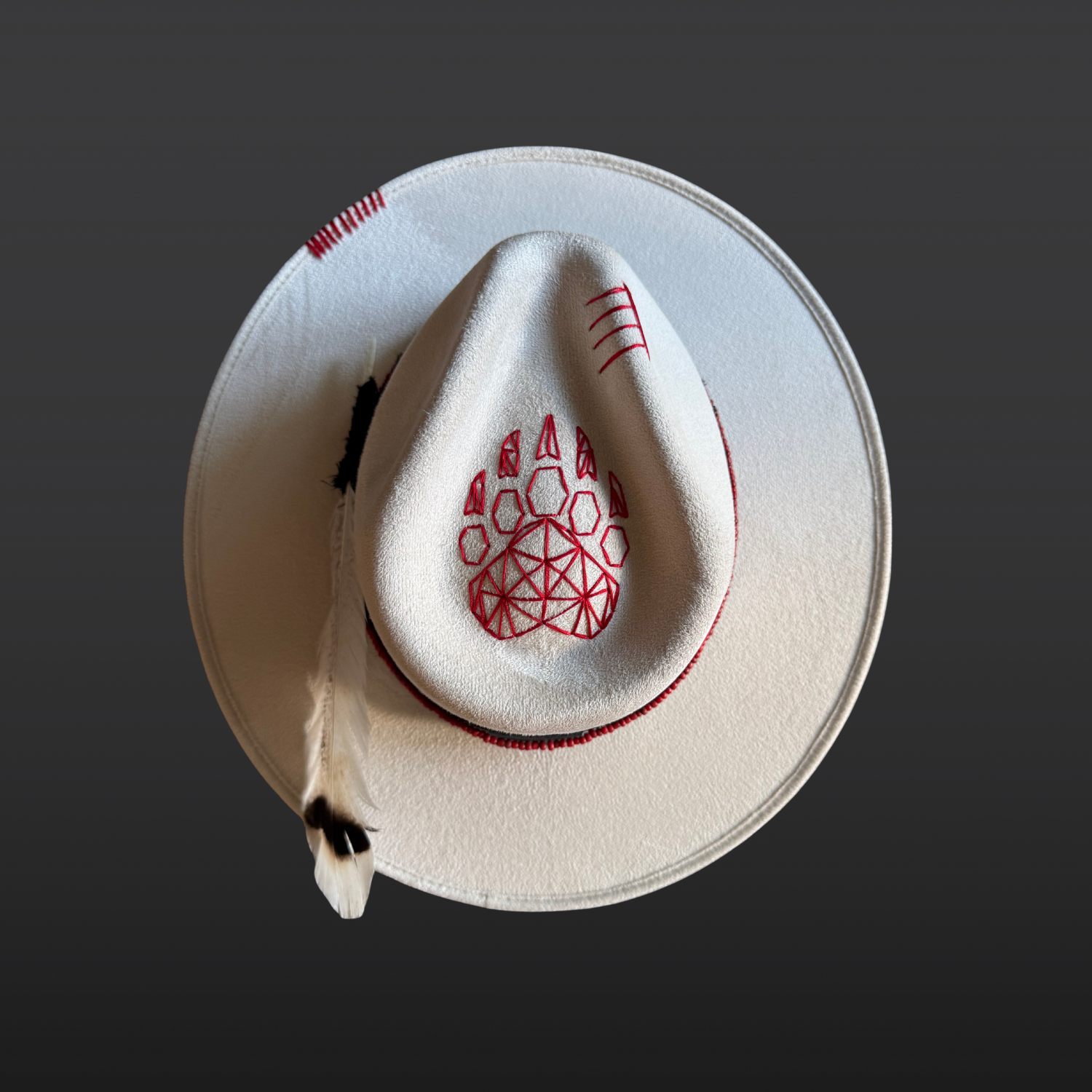 Top view of an ivory statement hat featuring a hand-embroidered red bear paw design.