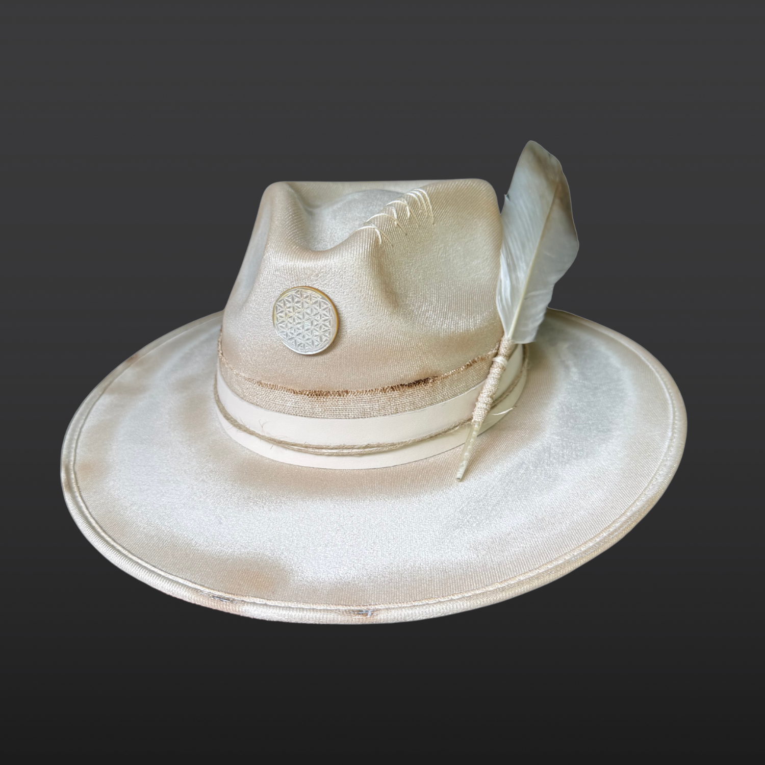 Burnished ivory wide-brim fedora by Inara Hat Co. featuring hand-burned detailing, a carved Flower of Life shell, layered organic bands, and an ethically sourced feather.