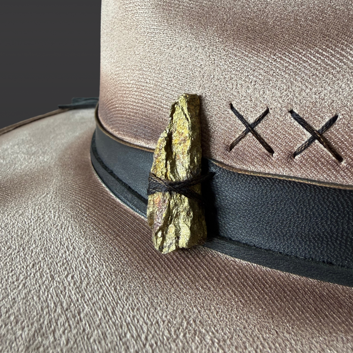 Crystal close-up:
A close-up of a metallic chalcopyrite crystal set against the black leather band of a khaki wide-brimmed fedora.