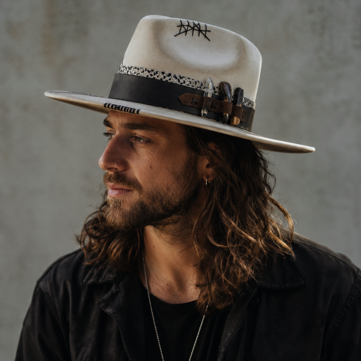 Unbound Fedora Hat worn by a street style man, showcasing the one of a kind wide brim fedora hat with ivory suede, black hatband, leather accents, bison tooth, palo Santo, clear quartz, feathers, and hand stitched details.