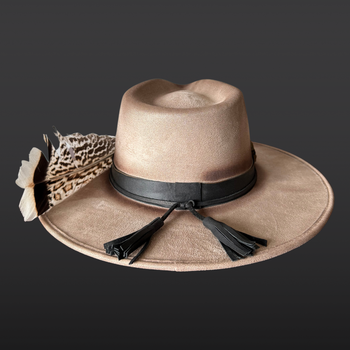 Back view:
A wide-brimmed khaki fedora shown from the back, featuring a black leather band with long flowing leather tassels and turkey feather accents.