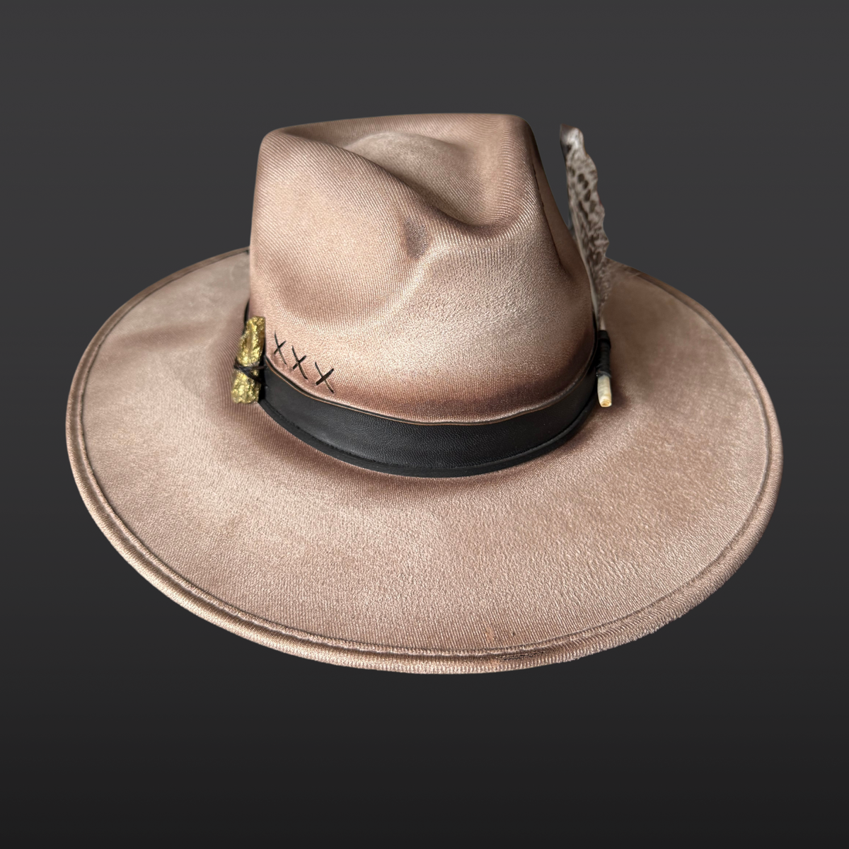 Left Side view:
A wide-brimmed khaki fedora featuring subtle hand-embroidered details, a chalcopyrite crystal, black leather band, and turkey feather accents.