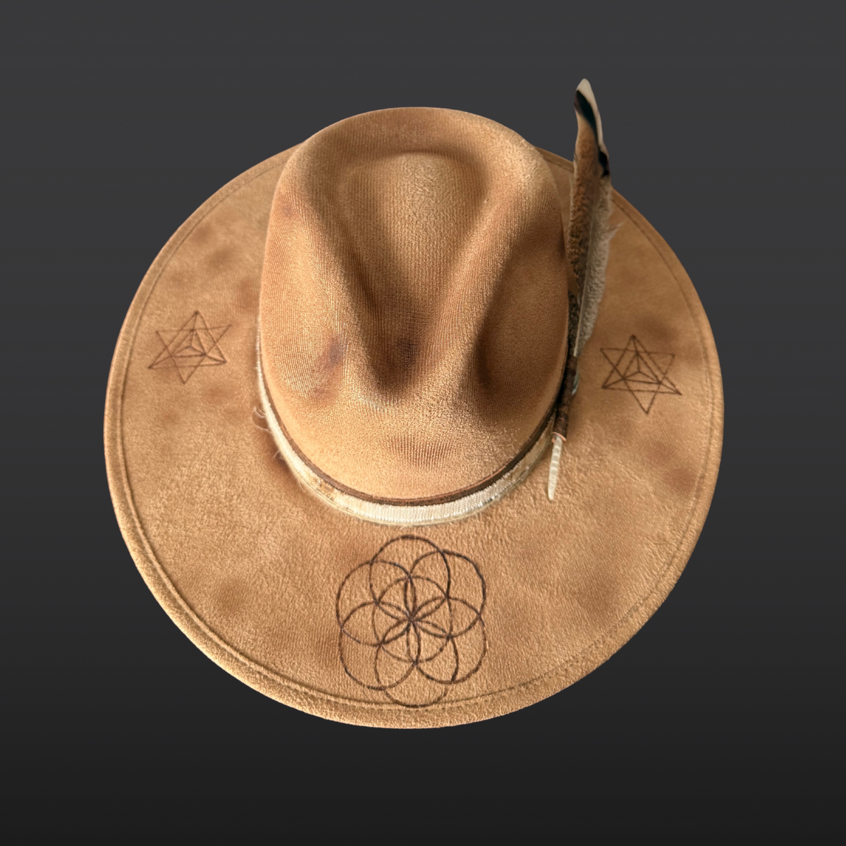 Top View:
A wide-brimmed camel-colored fedora shown from the side, featuring a dark brown leather band, agate stone, turkey feather accent, and hand-burned geometric designs on the crown.