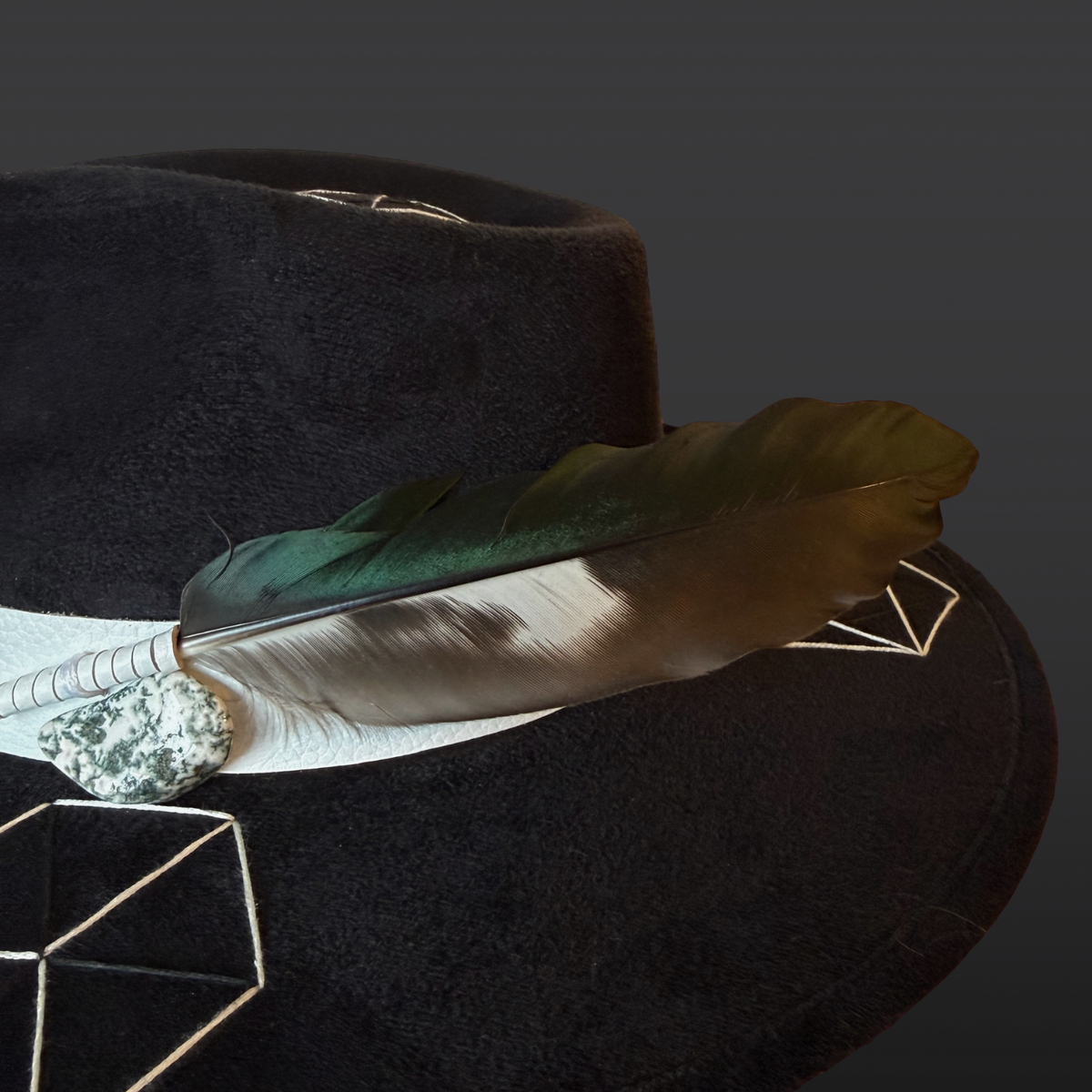 Crystal close-up:
A close-up of the vibrant green tree agate crystal attached to the white leather band of a black wide-brimmed fedora.
