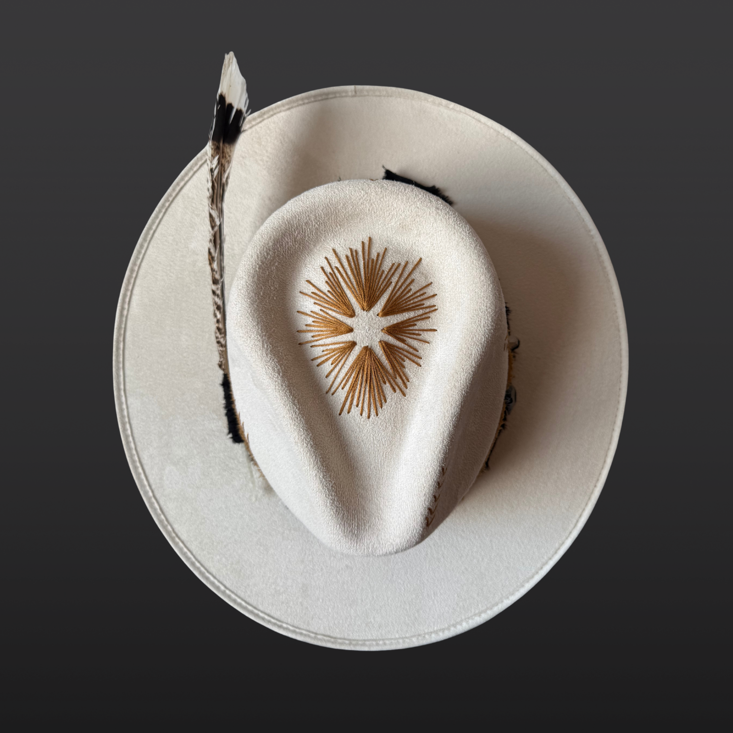 Top View of ivory wide-brim fedora hat with sunburst embroidery, Lumerian quartz, obsidian arrow, leather band and feather detail