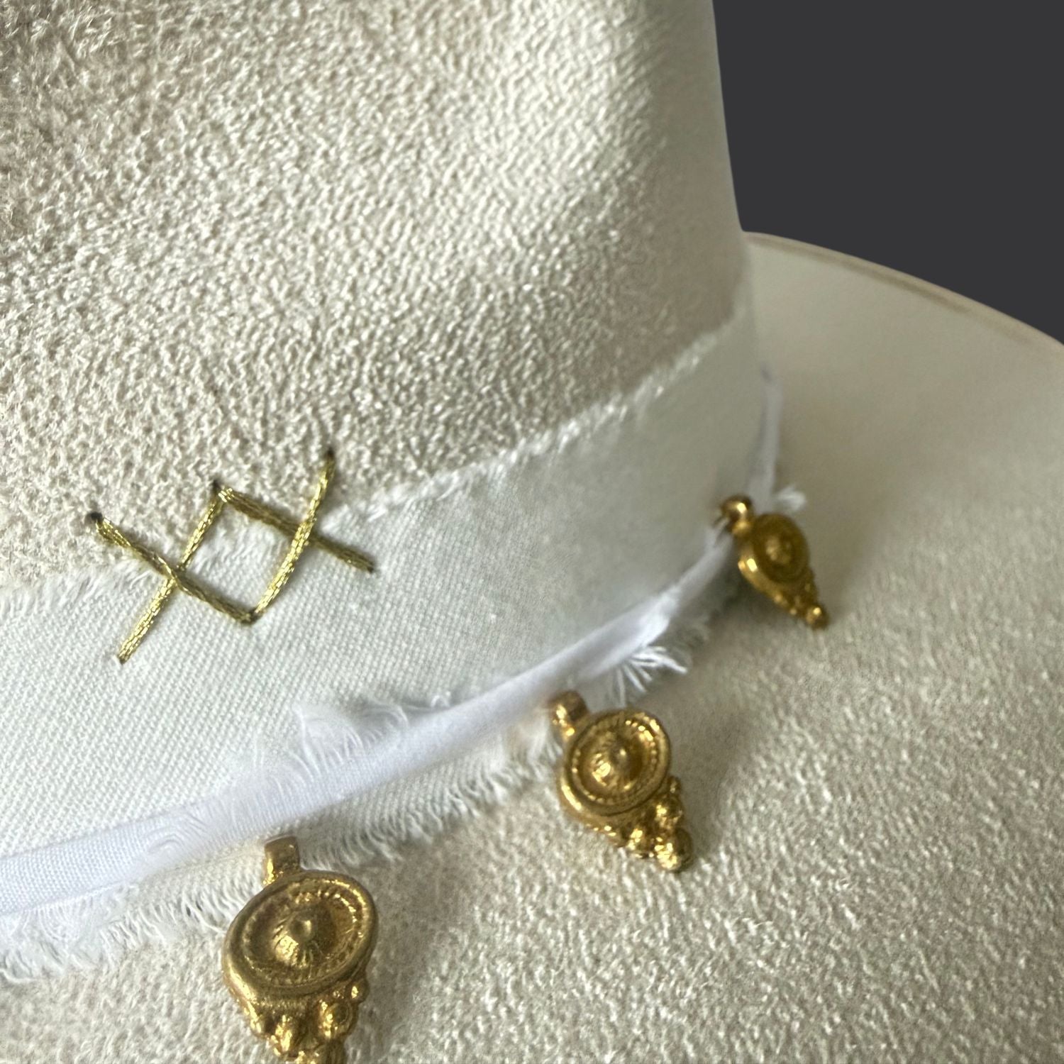 Ivory wide-brim fedora with gold hand-painted designs, white cotton band, and gold charm accents /close up of gold charms