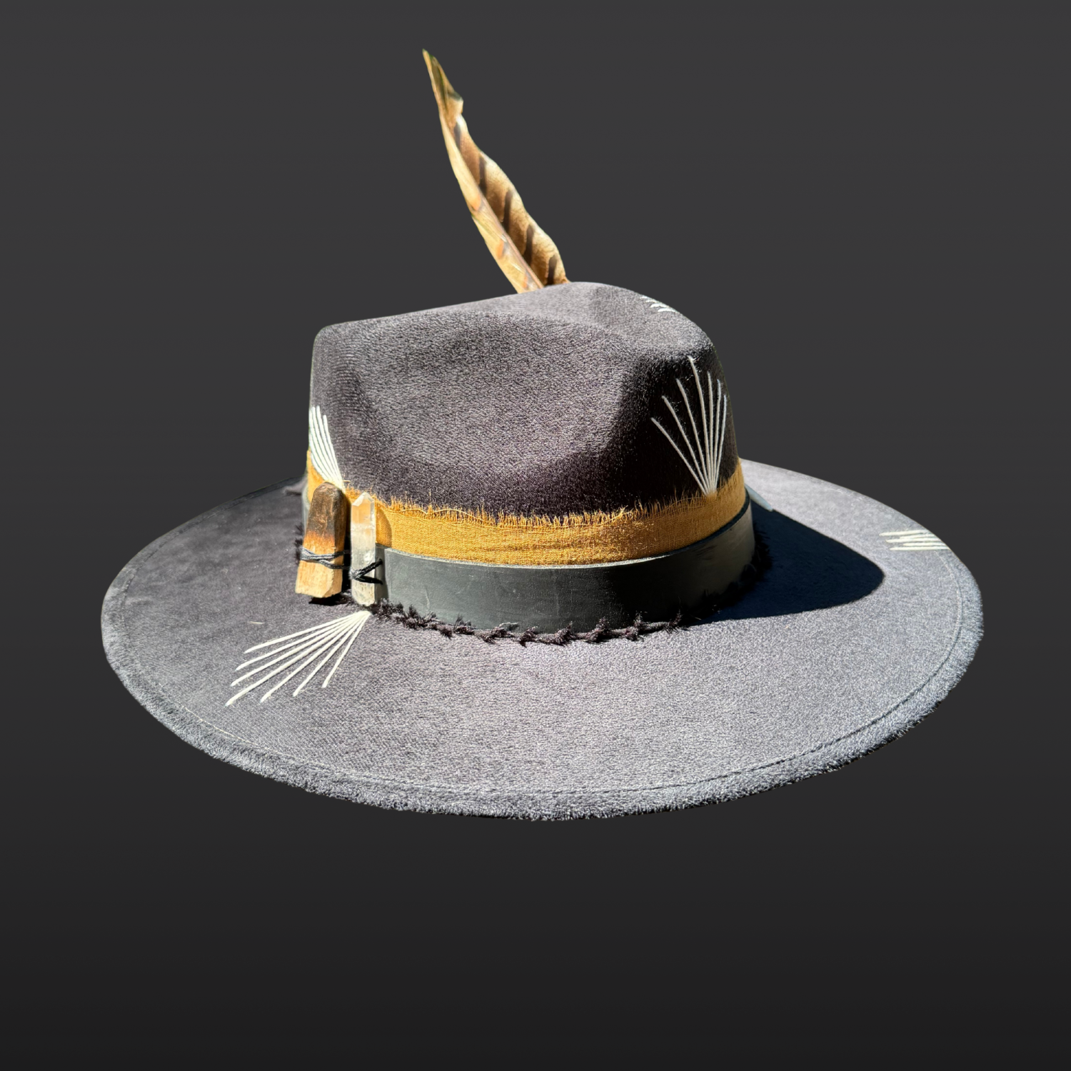 Side view of black wide brim fedora featuring Lemurian quartz crystal, burnt palo santo, black leather band, tobacco cotton band, and pheasant feather.