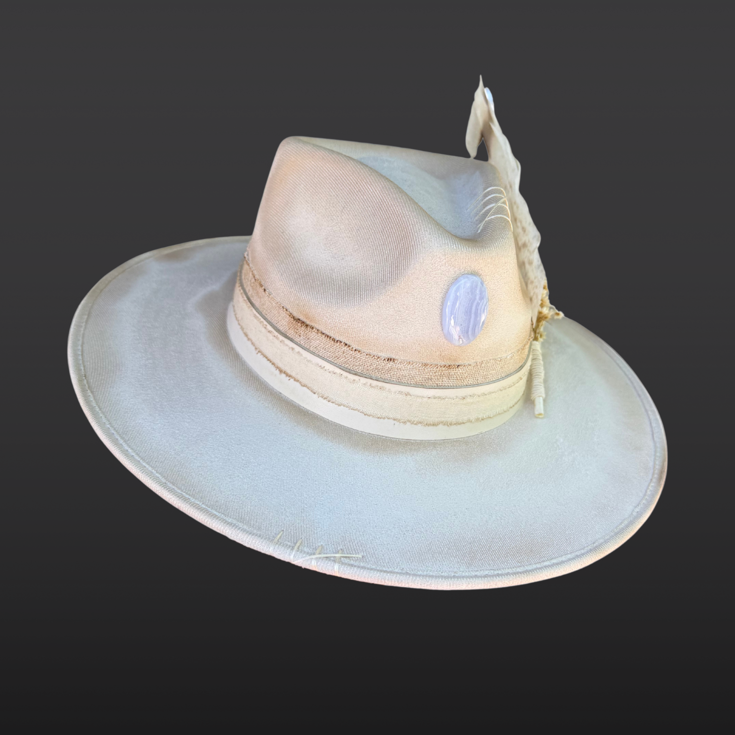 Side view of ivory wide brim fedora with blue lace agate crystal centerpiece, hand embroidered details, ivory leather band, and floral feather accents.