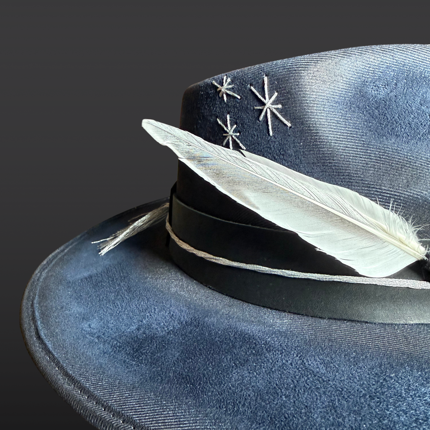 Close-up of hand-embroidered silver starburst designs and silver feathers on the Celestial Alignment Fedora Hat.