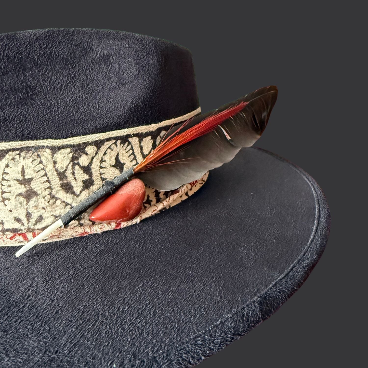 Close up of red jasper stone on black fedora with hand block printed cotton band and red stitching
