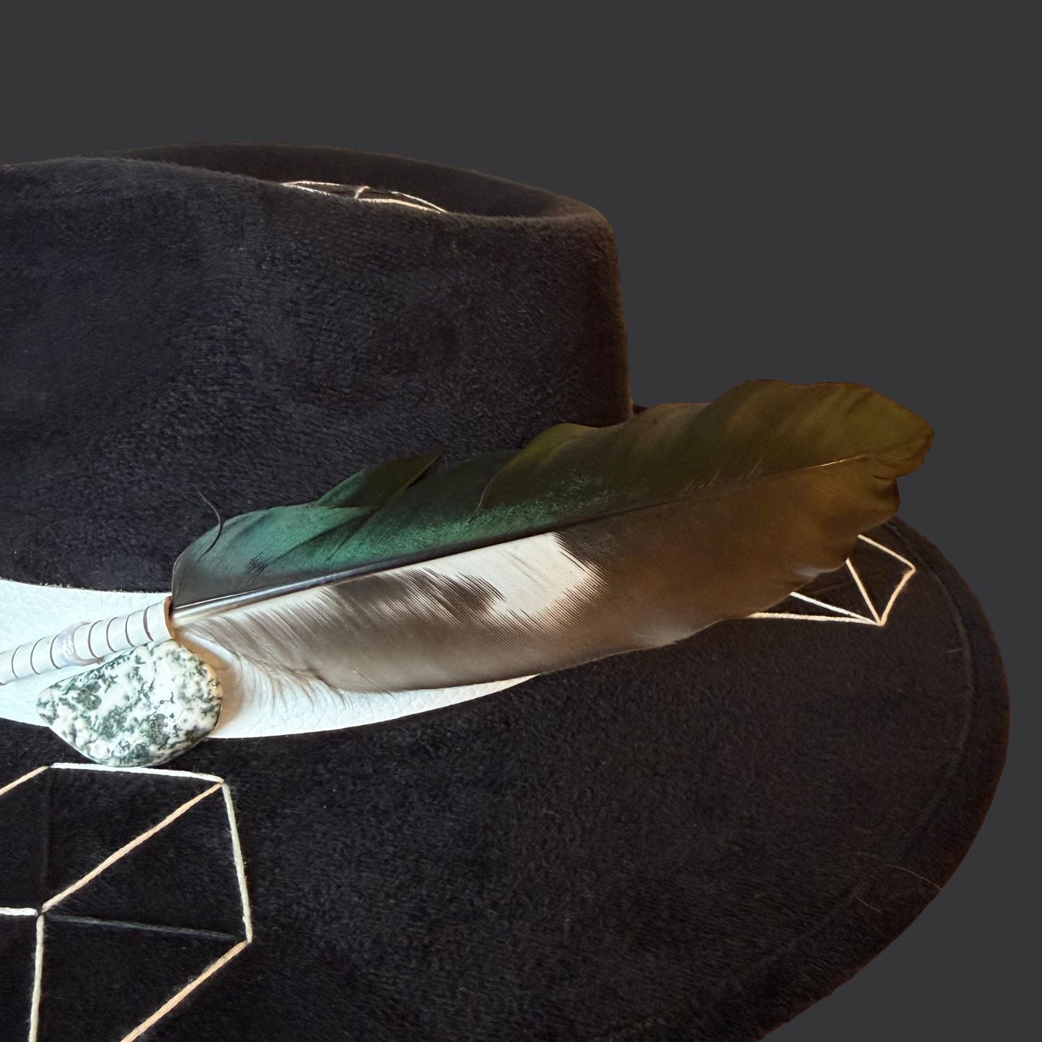 Black suede wide brim fedora with tree agate crystal, white leather band, and green black white duck feather / close up of crystal