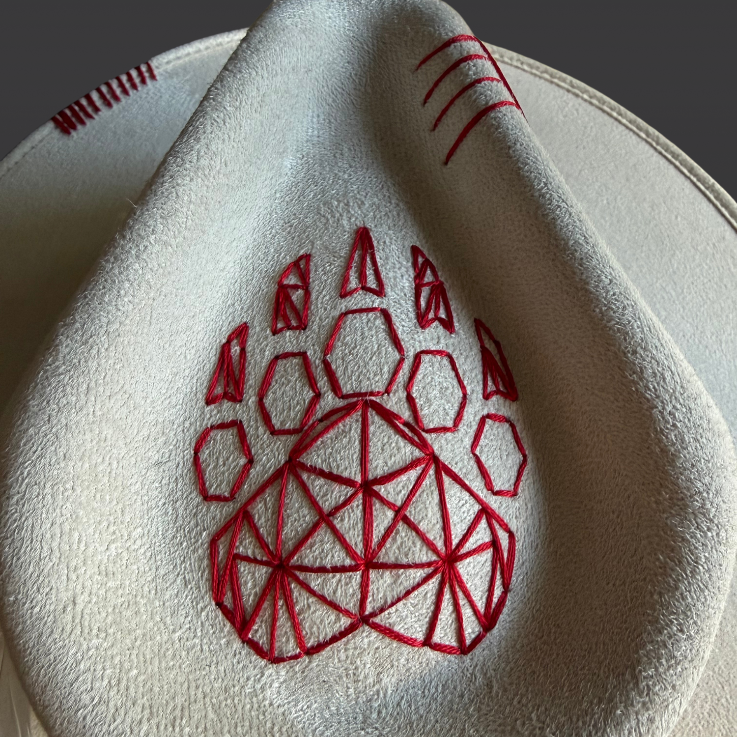 Close-up of the geometric bear paw embroidery stitched in red on the crown of the hat.