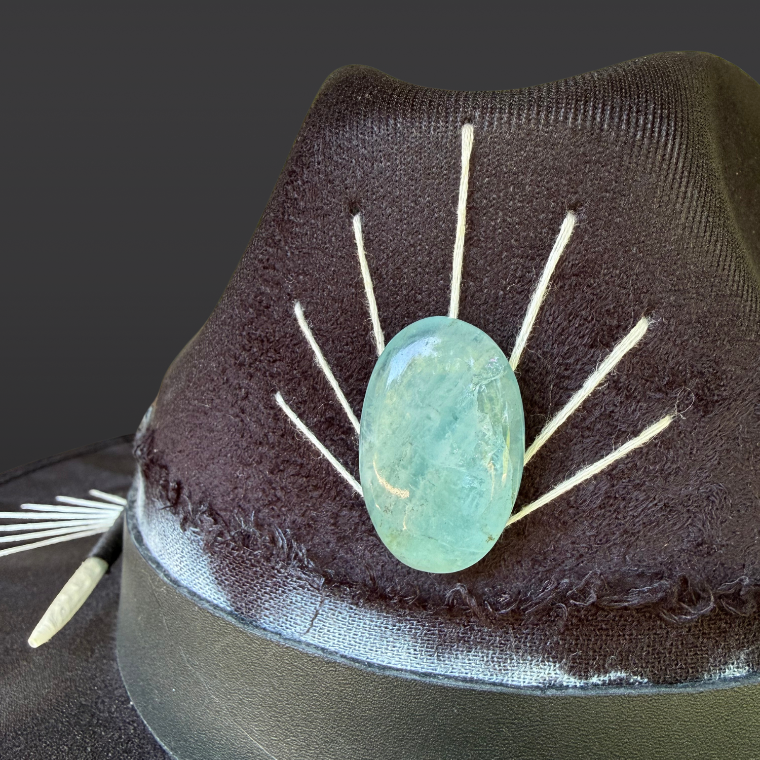 Close up of Aquamarine stone on Ocean Within black wide brim fedora with aquamarine stone, black leather band, aqua and turquoise cotton band, turkey feather, and hand embroidered accents by Inara Hat Co.