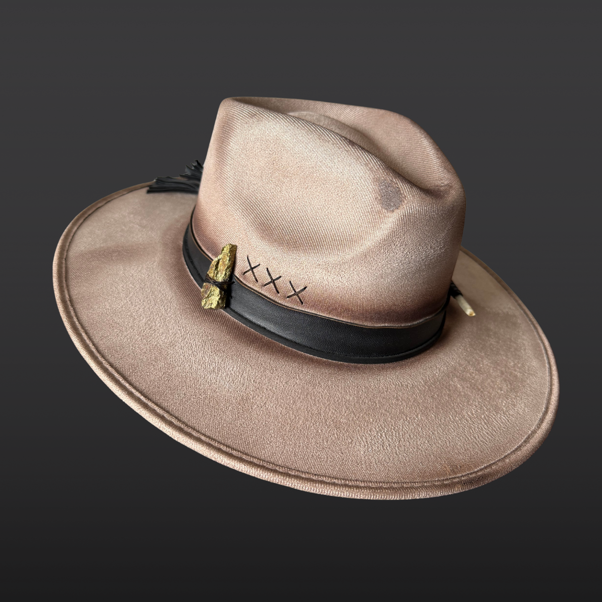 Main view:
A wide-brimmed khaki fedora featuring a hand-torched textured finish, black leather band with flowing tassels, hand-embroidered details, chalcopyrite crystal, and turkey feather accents.