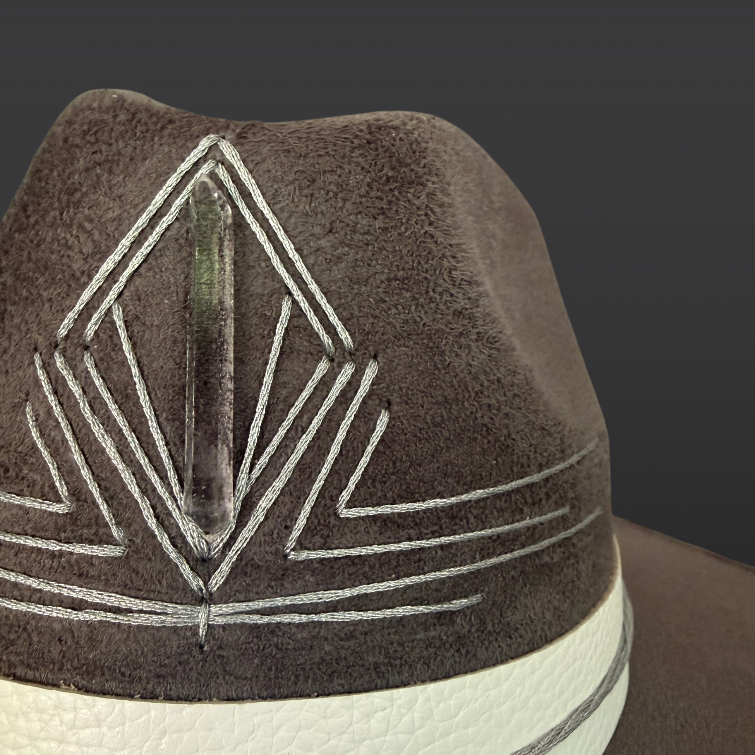 Close-up of the hand-embroidered silver triangle and Lemurian quartz on the crown of the gray fedora hat.